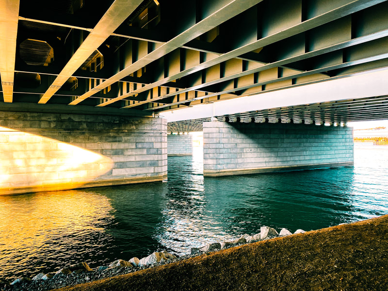 The underside of a bridge with water below. Golden beams from a setting sun project onto the white brick and steel beams.