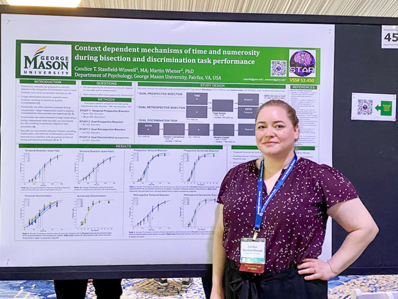 Candice, a white woman, is standing in front of her research poster at a conference. She is wearing a purple blouse and black slacks.
